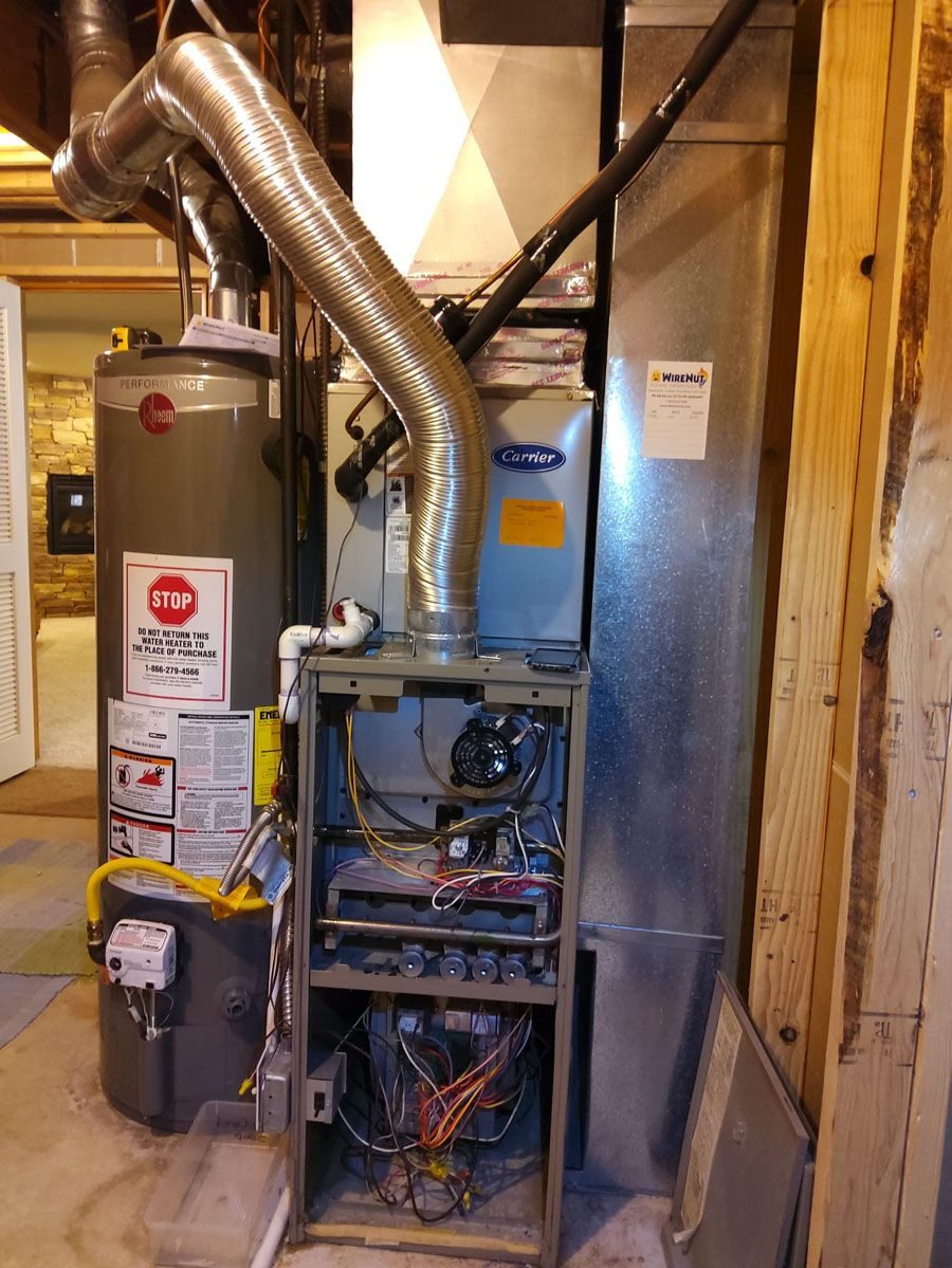 Furnace and tall water heater in a basement utility area with exposed ductwork and wiring nearby.