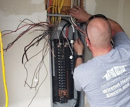 Electrician standing at an open breaker panel, organizing and connecting numerous wires in a utility box.