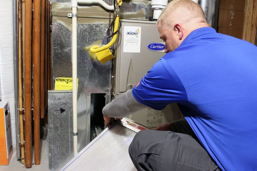 HVAC technician in a blue polo kneeling by a Carrier furnace, performing maintenance in a utility room.