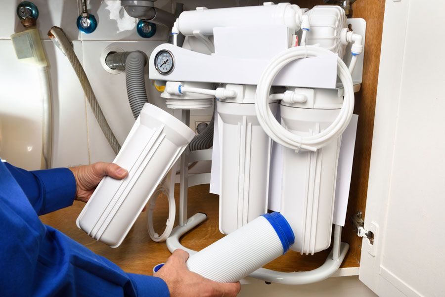 Person in a blue shirt replacing filters on an under-sink water filtration system.