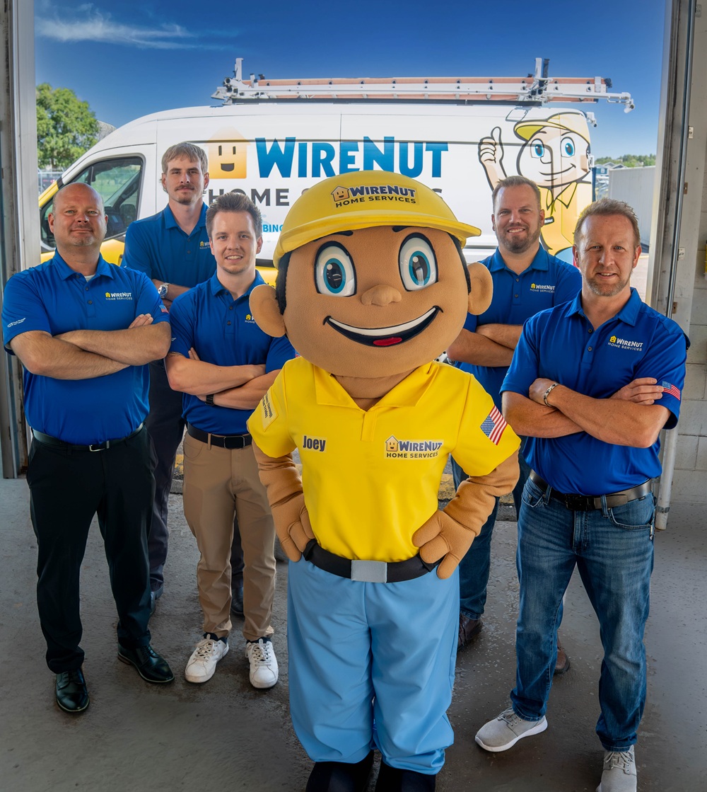 Team photo of WireNut Home Services crew and mascot Joey in a yellow uniform, standing with arms crossed in front of a company van.